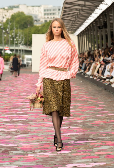 A model walking with a pink top and tweed skirt, holding a basket of flowers at Chanel couture 2023 show
